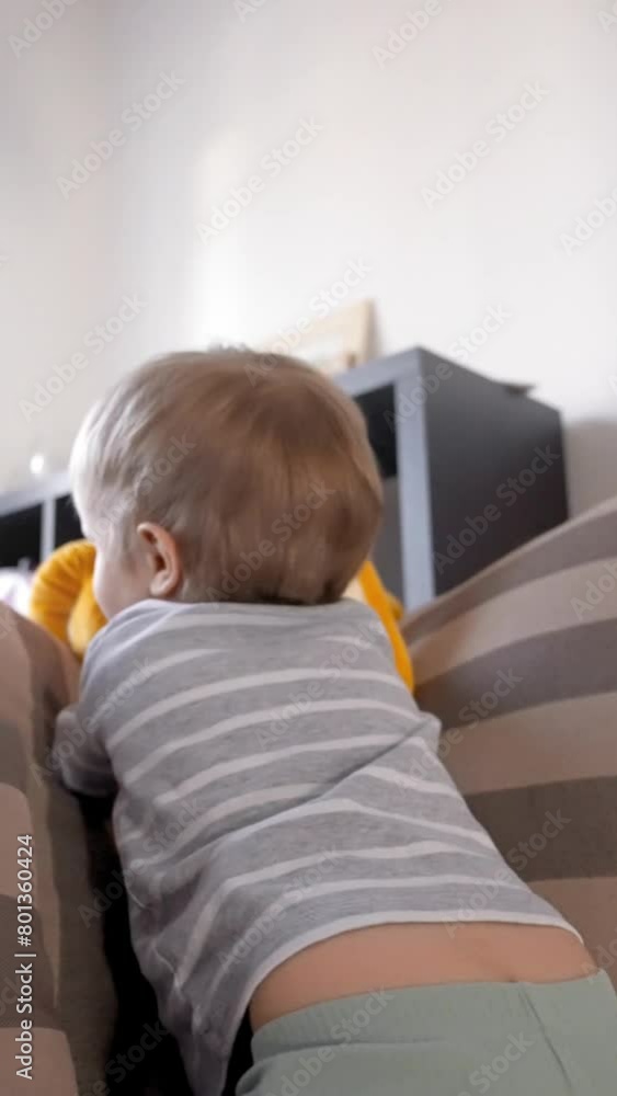 The toddler with bangs is sitting on the couch, gazing at a stuffed animal. The baby is wearing a tshirt with fur sleeves