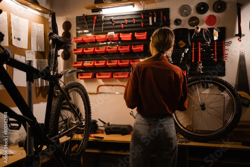 Rear view of a young woman in a garage. Bicycle repair and maintenance concept