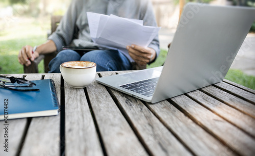 Asian man working outdoor on old wooden table with coffee drink checking business documents and using laptop working online