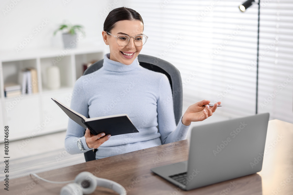 Young woman in glasses using video chat during webinar at table in office Young woman in glasses using video chat during webinar at table in office
