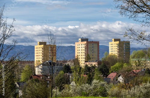 Tall buildings against a backdrop of mountains surrounded by greenery on a bright spring day