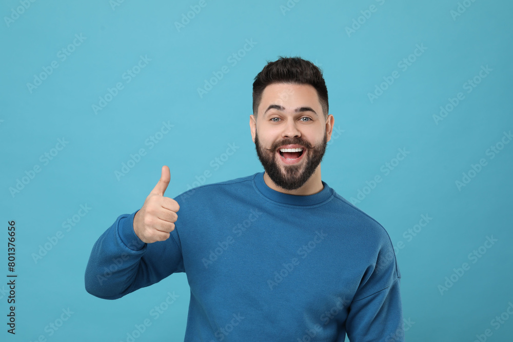 Happy young man with mustache showing thumb up on light blue background Happy young man with mustache showing thumb up on light blue background