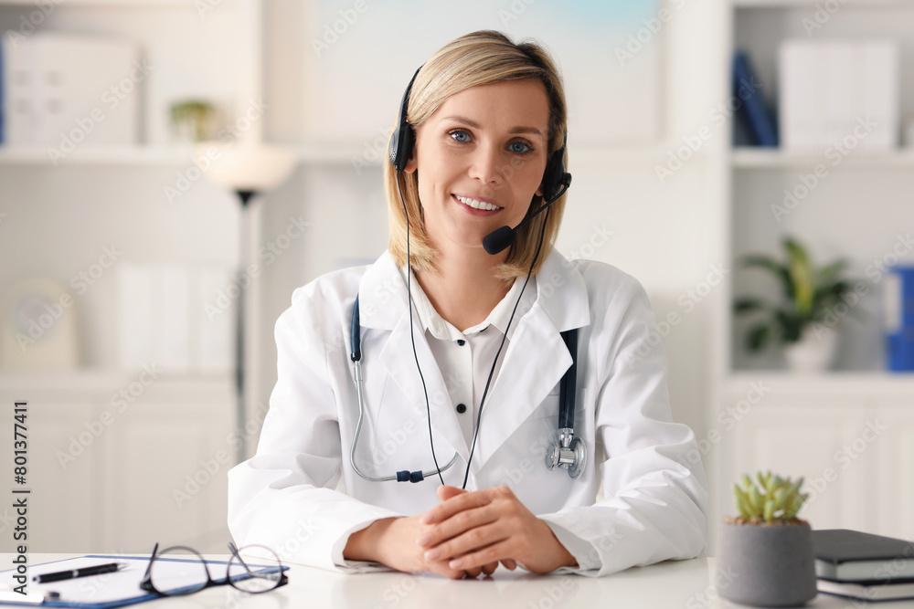 Portrait of smiling doctor in headphones having online consultation at table indoors Portrait of smiling doctor in headphones having online consultation at table indoors