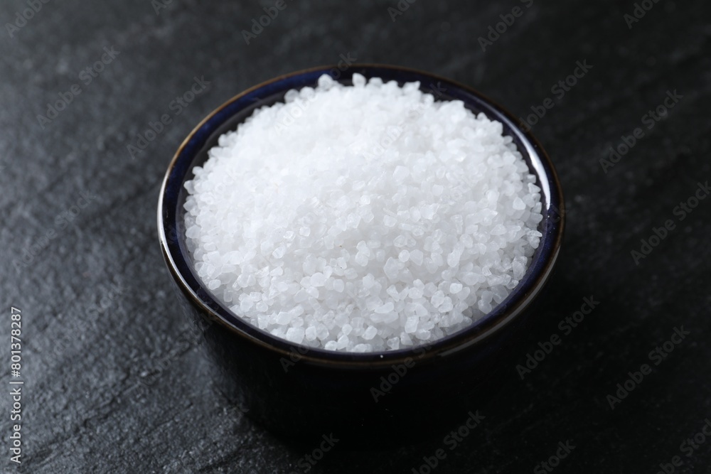 Organic white salt in bowl on black table Organic white salt in bowl on black table