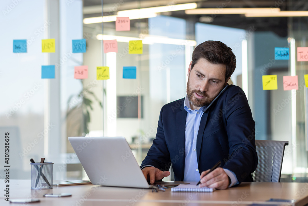 Focused businessman with beard using smartphone at a bright office desk, surrounded by colorful sticky notes on glass. Focused businessman with beard using smartphone at a bright office desk, surrounded by colorful sticky notes on glass.