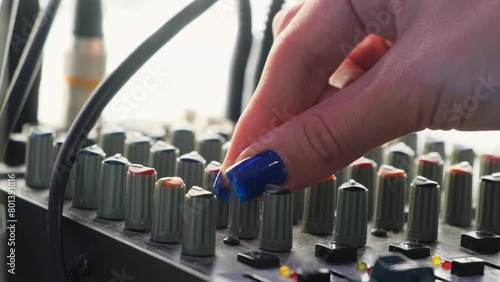 Female hand turns rotary knobs on mixer console in musical studio. Woman musician prepares equipment for recording session slow motion photo