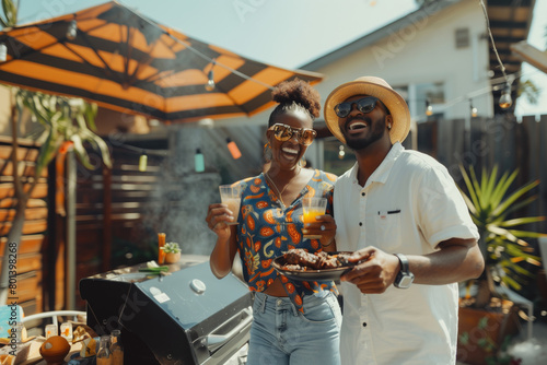 Joyful African American couple hosting a backyard barbecue party, sharing food and drinks on a sunny day. © KirKam