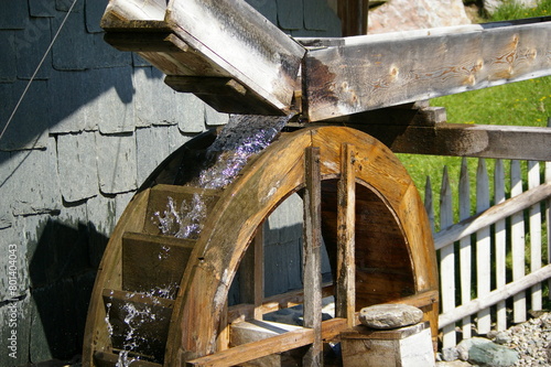 Fotografi Fresh flowing cold clear water running over a wooden waterwheel in the sunlight