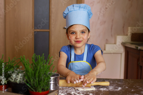 Foto Happy 5 year old girl in casual and dressed as chef in home kitchen rolling out