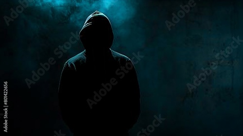 Mysterious figure in a hoodie standing in the dark, face obscured by shadow.