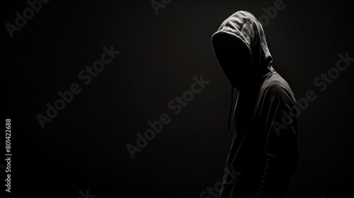 Mysterious figure in a hoodie standing in shadows, with a dark background and dramatic lighting.