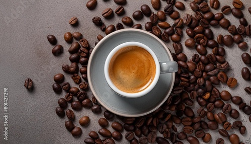 top view of a steaming cup of espresso amidst scattered coffee beans on a neutral background