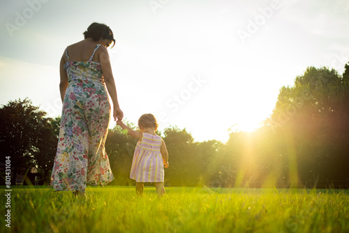 Mother and little daughter walking together in a park outdoors at sunset. evocative scene, concept of growing up together in parenthood, sharing happy moments together.
