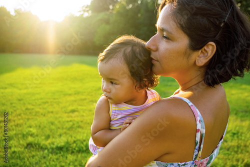 young mother holding cute baby daughter at sunset in nature looking in the same direction. concept of harmony in maternity and motherhood, sharing quality time