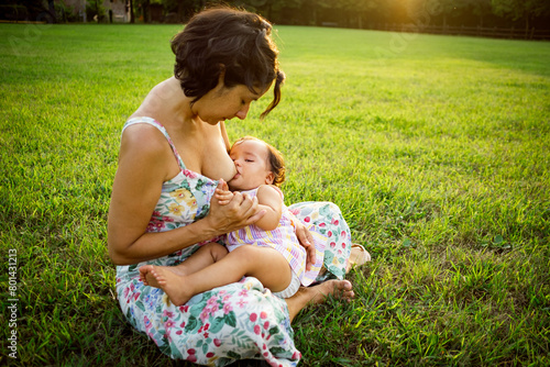 Young mother breastfeeding baby daughter in public park at sunset .concept of harmony in maternity and motherhood, sharing happy moments together.