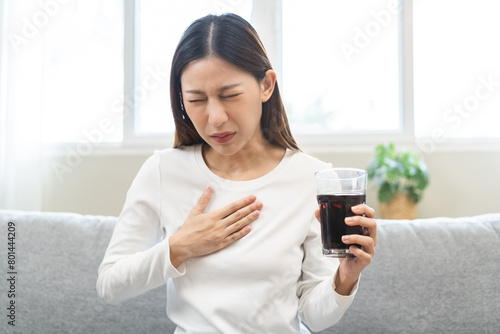 Acid reflux disease, suffer asian young woman, girl hand holding a glass of cola, have symptom gastroesophageal, heartburn pain on chest when drinking sparkling, soft water. Healthcare medical concept