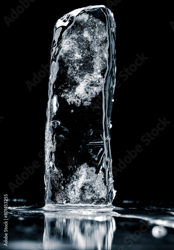Crystal clear frosty textured natural ice block with cracks on black mirroring surface.