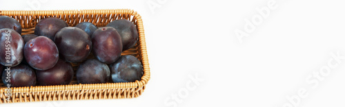 round blue plums in a basket on a white background. ripe sweet plums on a light texture	