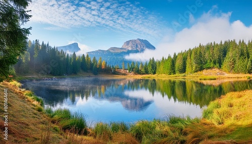 fabulous misty morning scene of nature view of forest lake in highland with rocky peak on background © Lauren