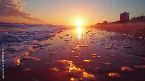   The sun sets on a beach with waves crashing  while in the distance  tall buildings loom behind it