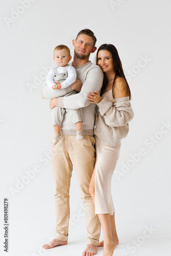 Mother and father hold a one-year-old son of a child in their arms. Portrait of a happy family with a baby in cozy casual clothes for home