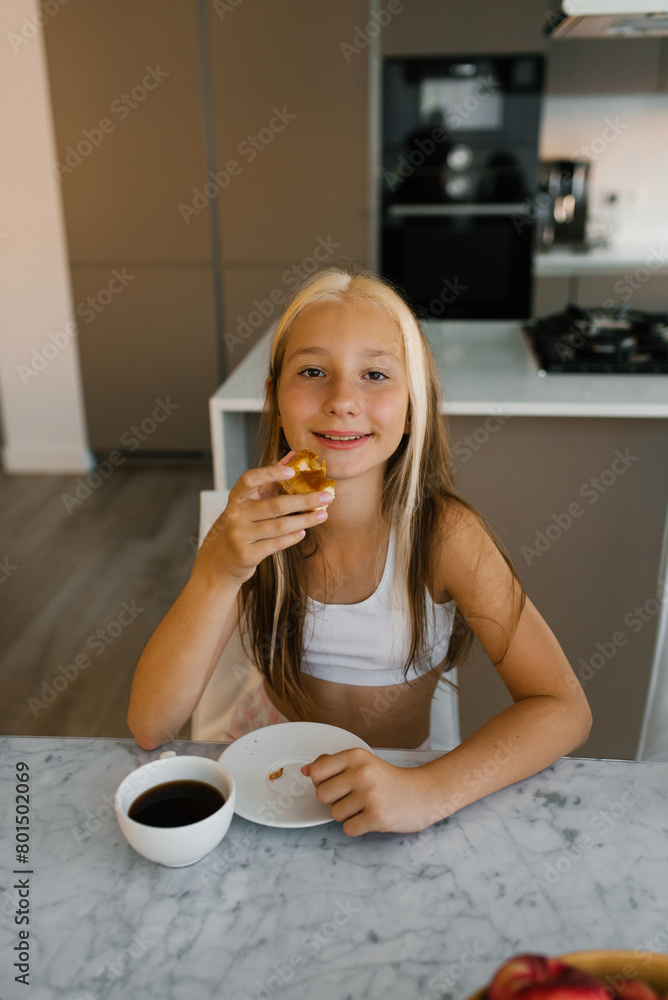 Cute teenage girl eats a piece of pie at the table in the kitchen and smiles Cute teenage girl eats a piece of pie at the table in the kitchen and smiles