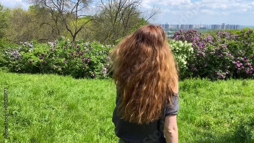 Red-haired beautiful girl walking on green grass in botanical garden.