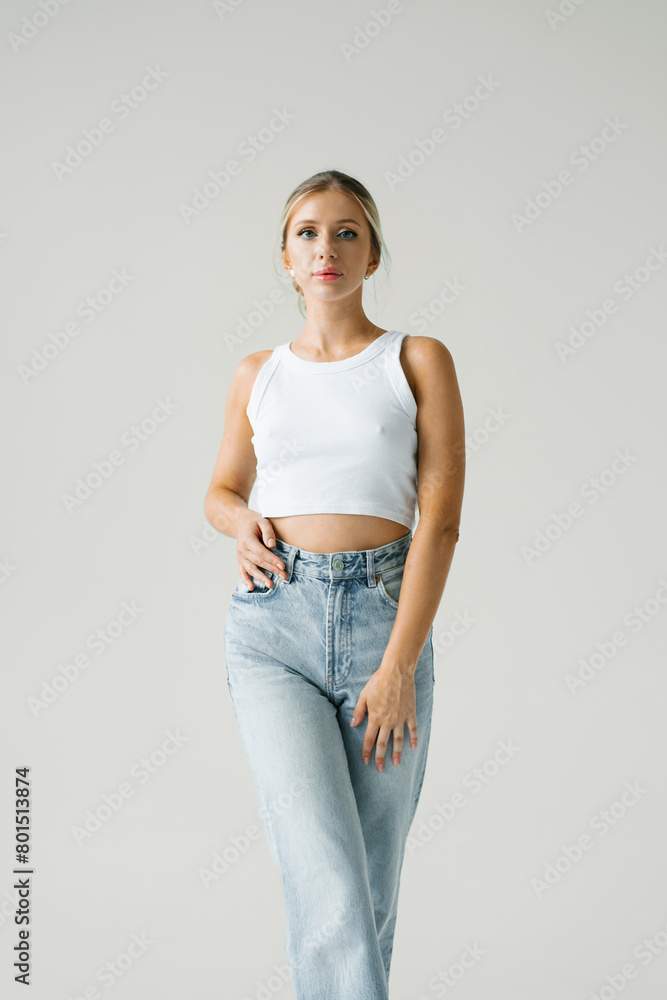 Young woman model is wearing a white tank top and blue jeans Young woman model is wearing a white tank top and blue jeans