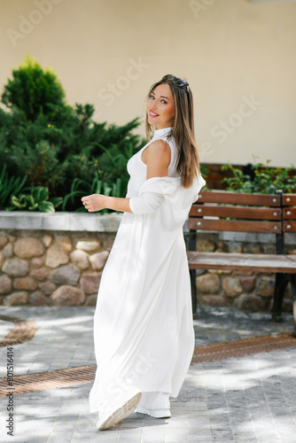 Happy woman in a white dress is standing in front of a bench