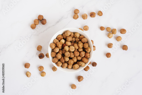 Hazelnut in a white bowl and are scattered on a marble table