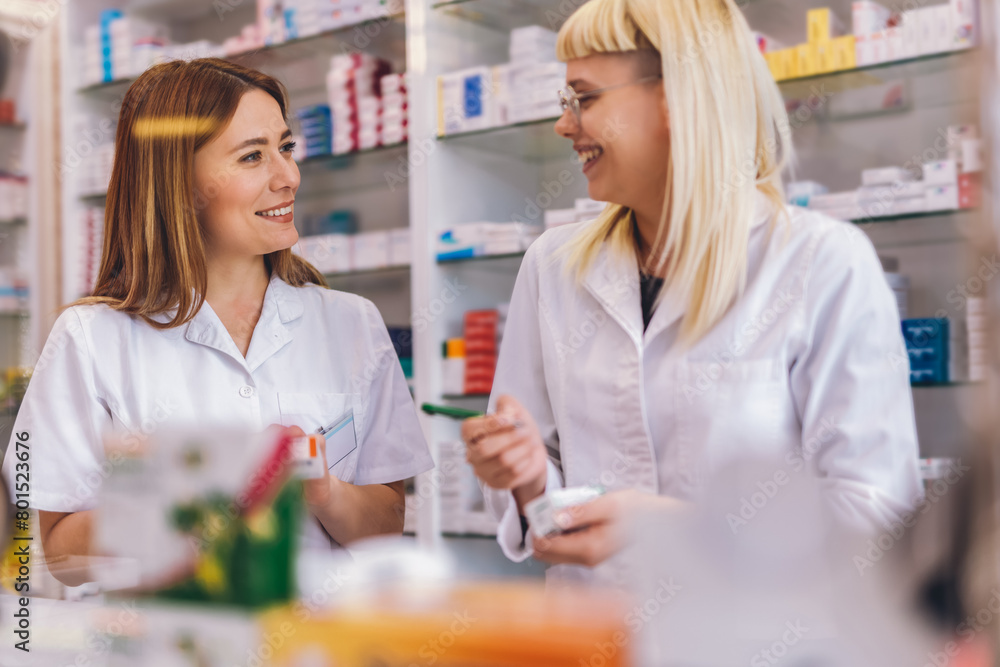 Two young pharmacists at the cash desk of pharmacy store. Talking about medicine.