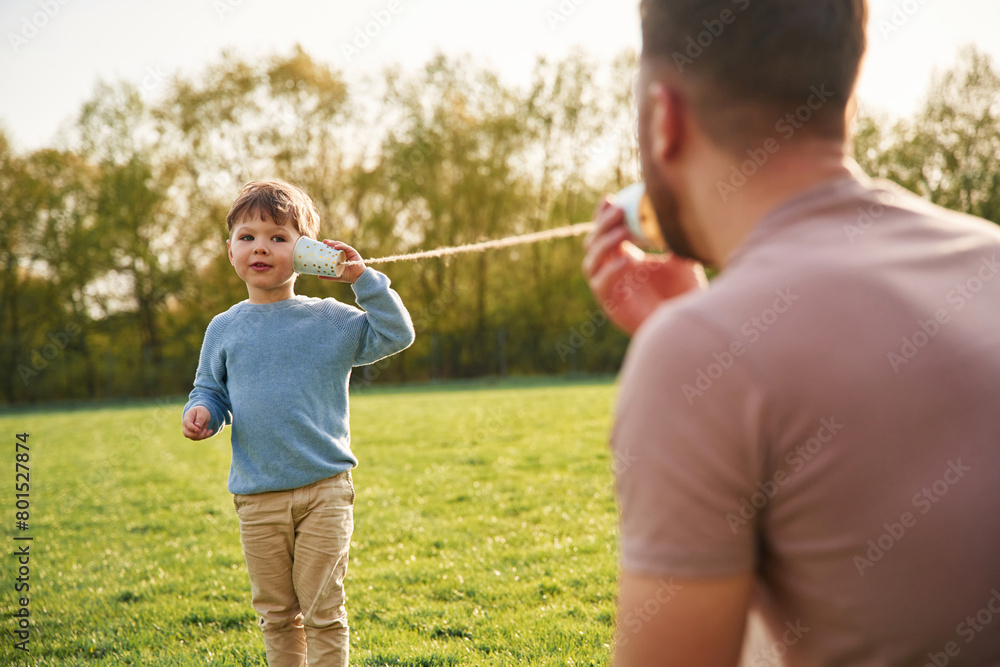 Using paper cup telephone. Happy father with son are having fun on the field at summertime Using paper cup telephone. Happy father with son are having fun on the field at summertime