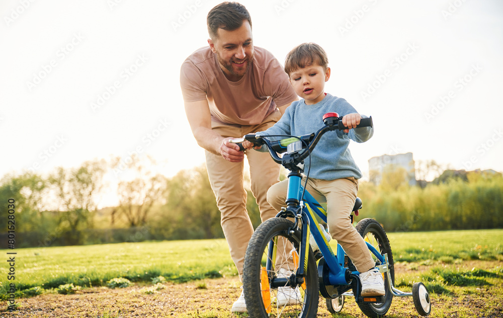 Fototapeta premium Trying the bicycle. Happy father with son are having fun on the field at summertime