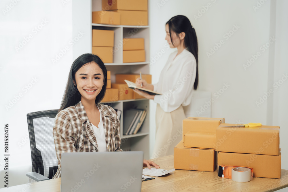 Asian businesswoman using laptop computer checking customer's shipping box online at home. SME startup. Small business entrepreneur, freelancer. Online business, SME work Asian businesswoman using laptop computer checking customer's shipping box online at home. SME startup. Small business entrepreneur, freelancer. Online business, SME work