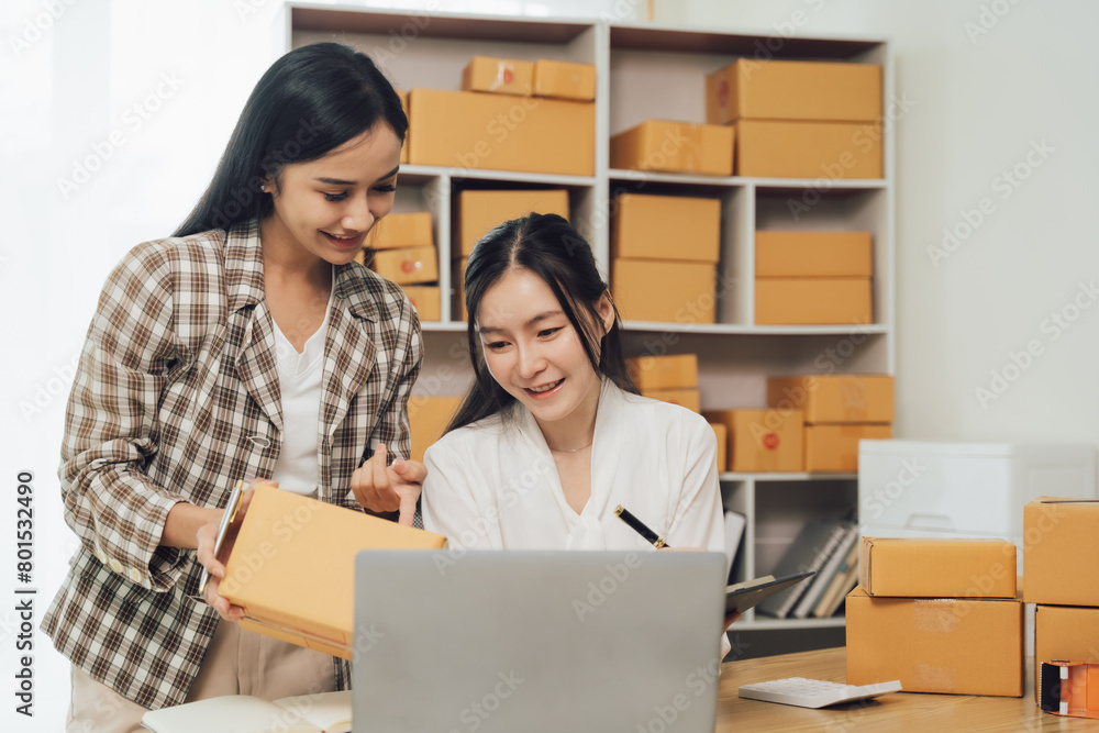 Asian businesswoman using laptop computer checking customer's shipping box online at home. SME startup. Small business entrepreneur, freelancer. Online business, SME work Asian businesswoman using laptop computer checking customer's shipping box online at home. SME startup. Small business entrepreneur, freelancer. Online business, SME work