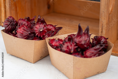 Cardboard square boxes filled with organic hibiscus sabdariffa or dried roselle flowers for sale. The tropical flora is vibrant red with a trumpet-shape edible herbal fruit having antioxidant powers. 