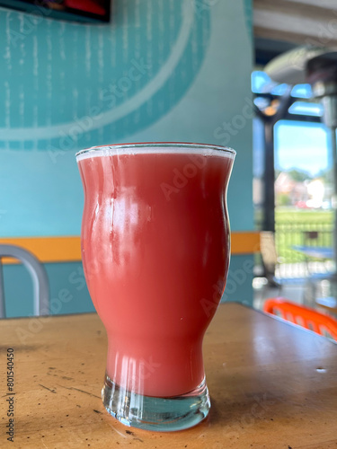 A clear nonic pint glass filled with a red berry flavored beer. The craft alcohol draught ale has a bold taste with a refreshing cold moisture on the outside of the glass and thick foam on top.  photo