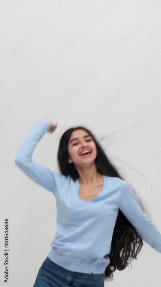 Dynamic, cheerful and optimistic young Indian woman playfully dancing to music on white background. Active entertainment concept. Vertical video. Dynamic, cheerful and optimistic young Indian woman playfully dancing to music on white background. Active entertainment concept. Vertical video.