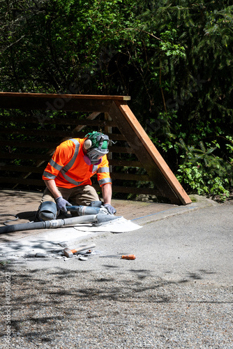 City parks workman grinding down concrete at the end of a bridge to level it off with the asphalt path for safety 