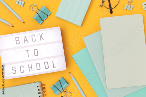 Back to school. Lightbox with letters and mint colored stationery on a yellow background.