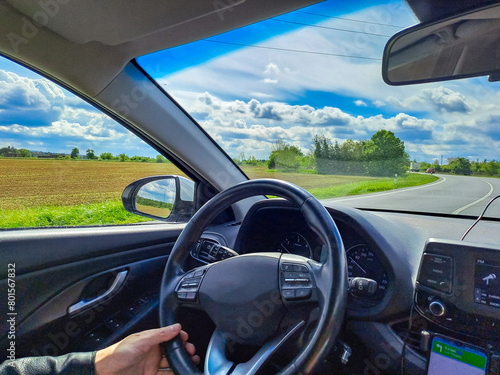 Man hands holding car steering wheel while driving through countryside landscape