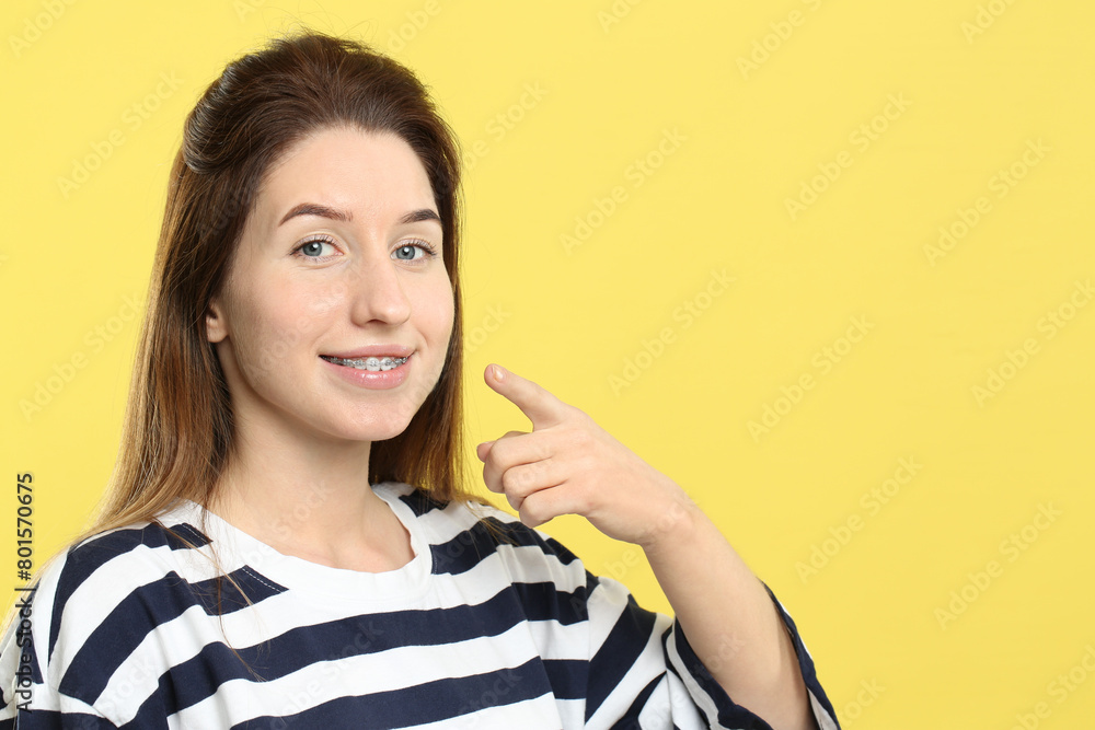 Smiling woman pointing at her dental braces on yellow background, closeup. Space for text Smiling woman pointing at her dental braces on yellow background, closeup. Space for text