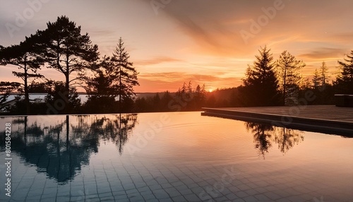 a pool with a view of trees and a sunset the water is calm and the sky is orange © Mac