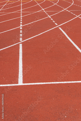Close-up of a red athletic track with white lane marking and granular texture, at an outdoor sports center in Paris © Marco B.