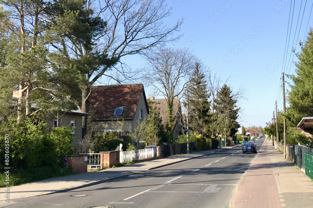 A vehicle is moving along a road surrounded by houses and trees in a residential area, with asphalt road surface under a clear sky