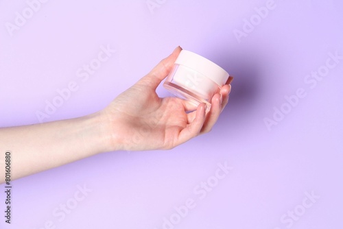 Woman holding jar of cream on violet background, closeup