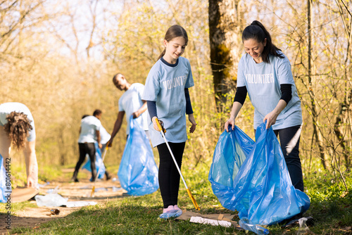 Sweet child and mother collecting trash and plastic in a disposal bag, recycling junk and cleaning the forest ecosystem. Young girl working with her mom to tidy up the nature.