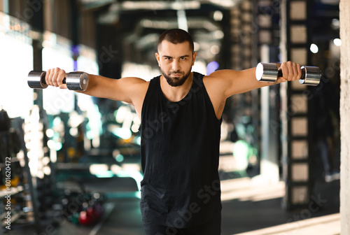 A man is standing while holding two dumbbells in his hands. He appears to be focusing on his workout routine, showcasing strength and determination.
