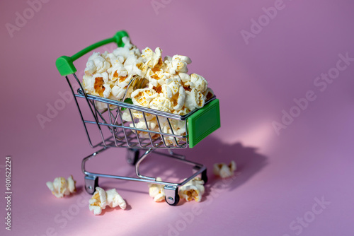 Freshly made popcorn in a shopping cart on a pink background