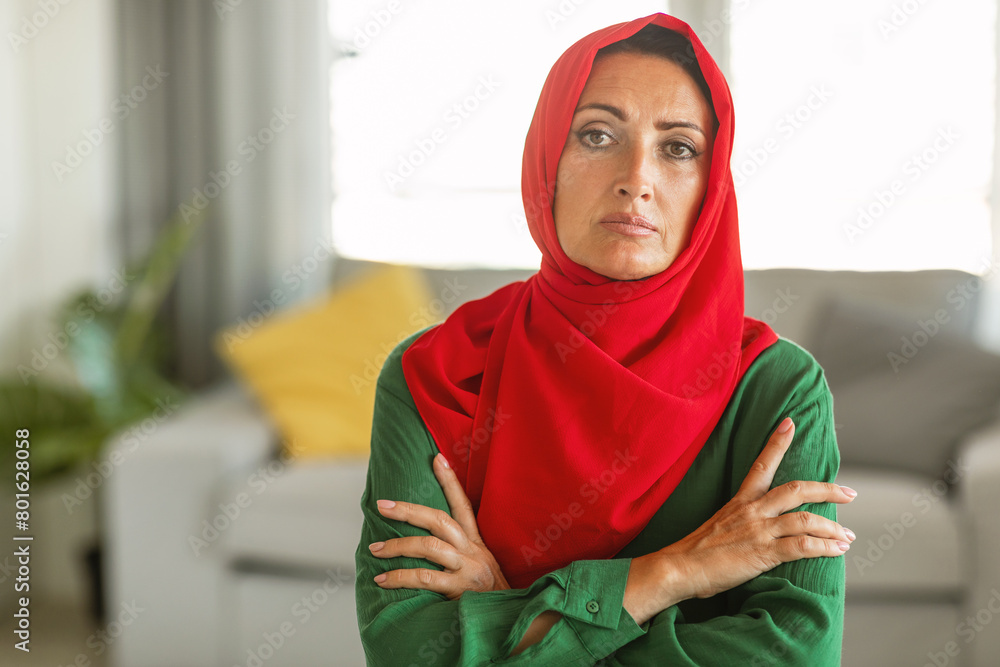 A woman is depicted wearing a hijab that is predominantly red with green accents. She appears to be looking directly at the camera, with a serene expression on her face. A woman is depicted wearing a hijab that is predominantly red with green accents. She appears to be looking directly at the camera, with a serene expression on her face.